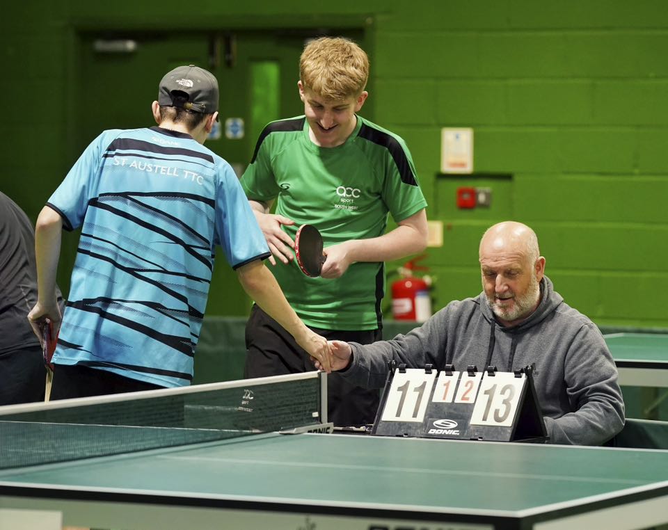 An umpire sits behind a close score and shakes hands with one of the players.