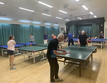 Several players play table tennis in a village hall