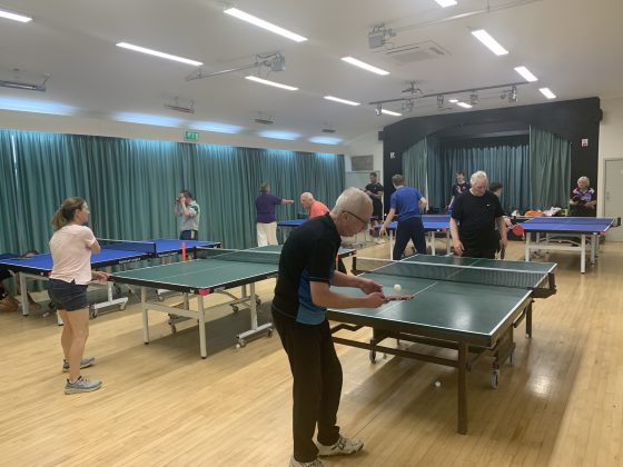 Several players play table tennis in a village hall