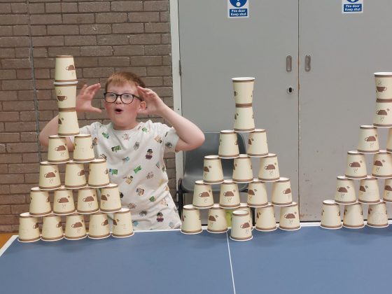 A boy is amazed at his achievement of building a large pyramid of coffee cups as a target on a table tennis table